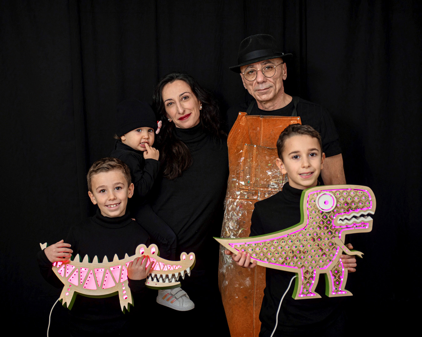 fotografia professionale personal branding di una famiglia di artigiani su fondo nero con due lampade in mano una a forma di coccodrillo e una a forma di dinosauro.